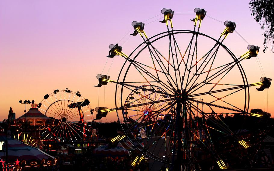 Ferris wheels and other carnival rides silhouetted against a purple and orange sunset